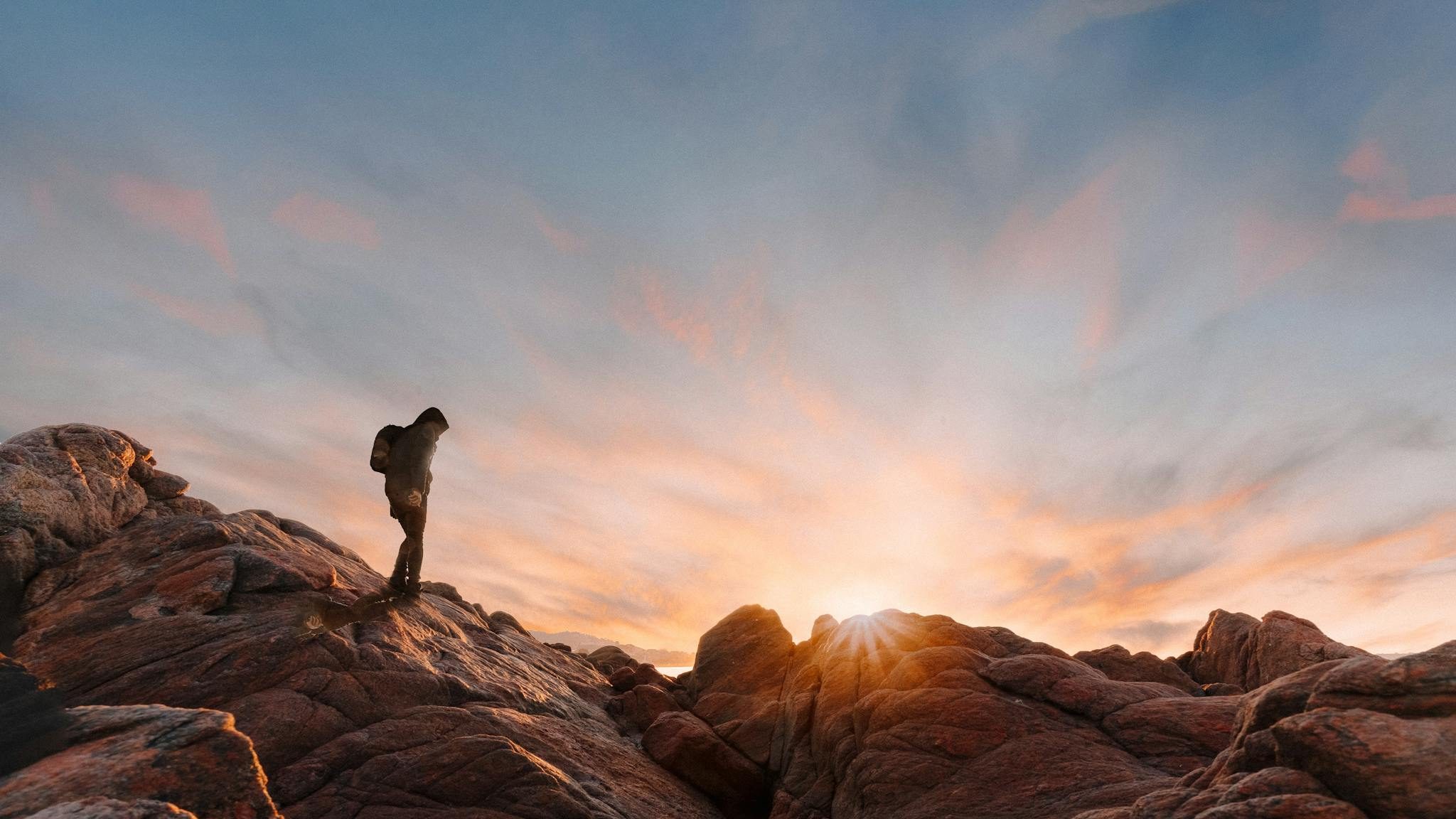 Picturesque view of vibrant sunset above unrecognizable tourist with backpack hiking through rocks